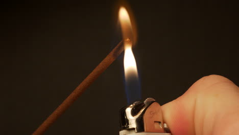 lighting the end of an incense stick with a lighter and gently blowing out the flame creating smoke and a red glow - close up shot