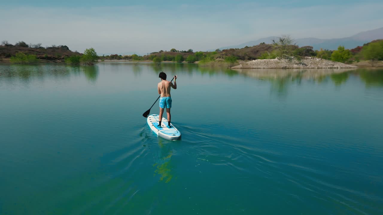 Uomo che fa paddleboard su un lago calmo con montagne sullo sfondo