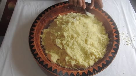 mujer rodando sémola caliente de cuscús con una cuchara en un plato de madera en casa después de cocinarlo al vapor