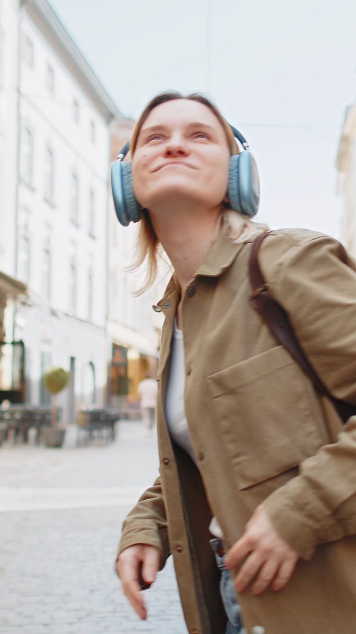 Vista posteriore di una giovane turista con uno zaino che ascolta musica con le cuffie mentre cammina per strada