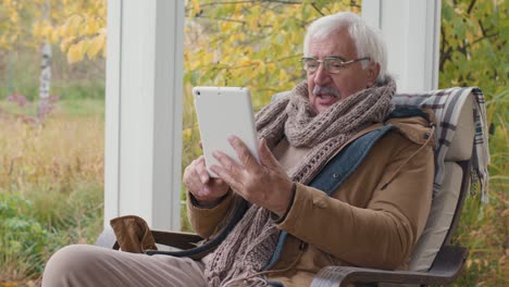 senior man sitting on a bench in home garden while talking on a video call using a tablet