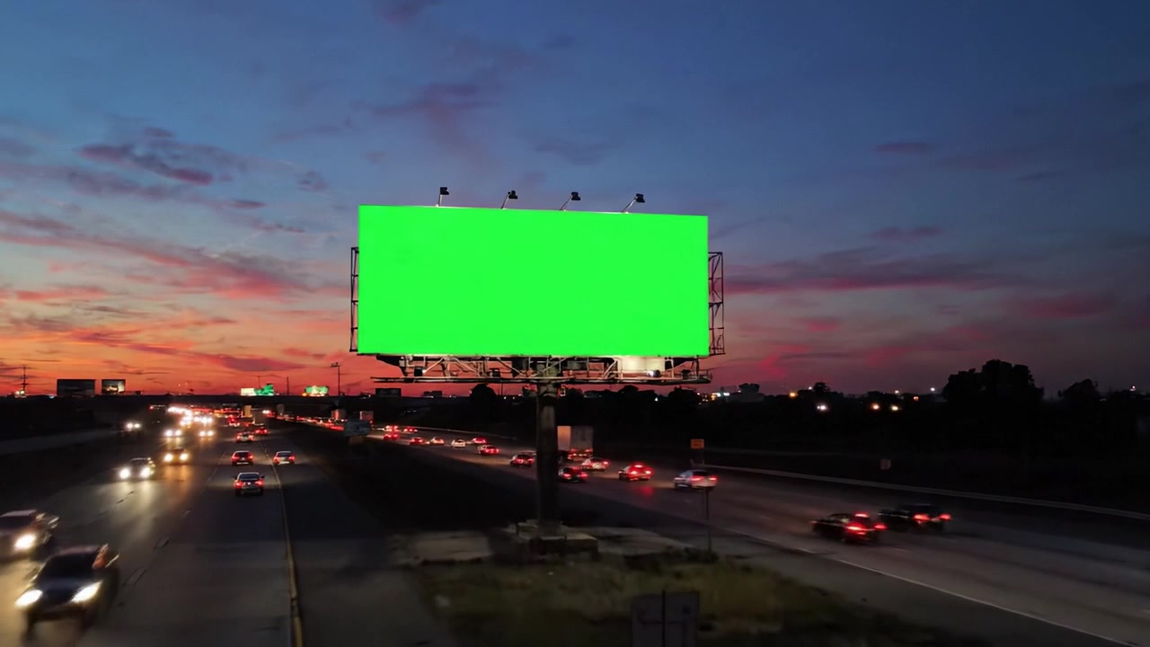 Una serie de vallas publicitarias con pantallas verdes vibrantes a lo largo de la autopista al atardecer y por la noche, reflejando la transición de la luz del día y la vida urbana