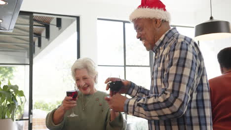 amigos mayores felices y diversos, hombres y mujeres, celebrando la navidad con vino en casa, en cámara lenta.