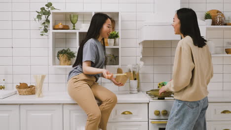 Two-Japanese-friends-in-the-kitchen.-One-of-them-is-sitting-at-the-counter-eating-takeaway-ramen-and-another-one-is-cooking-on-the-fire