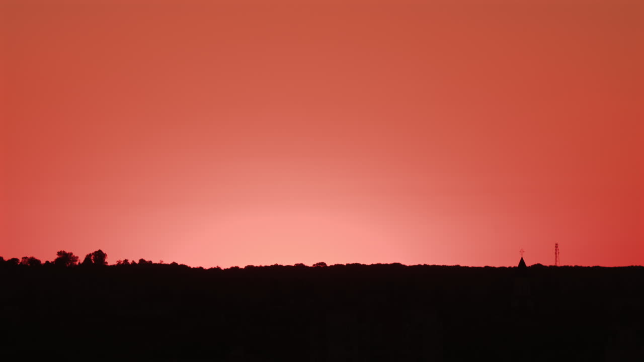 Stunning sunset with the sun descending behind the hills and a bird flying across the orange sky