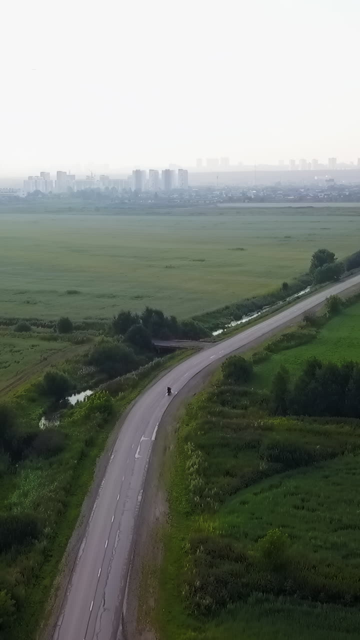 Aerial view of a road passing through a green field towards a city skyline