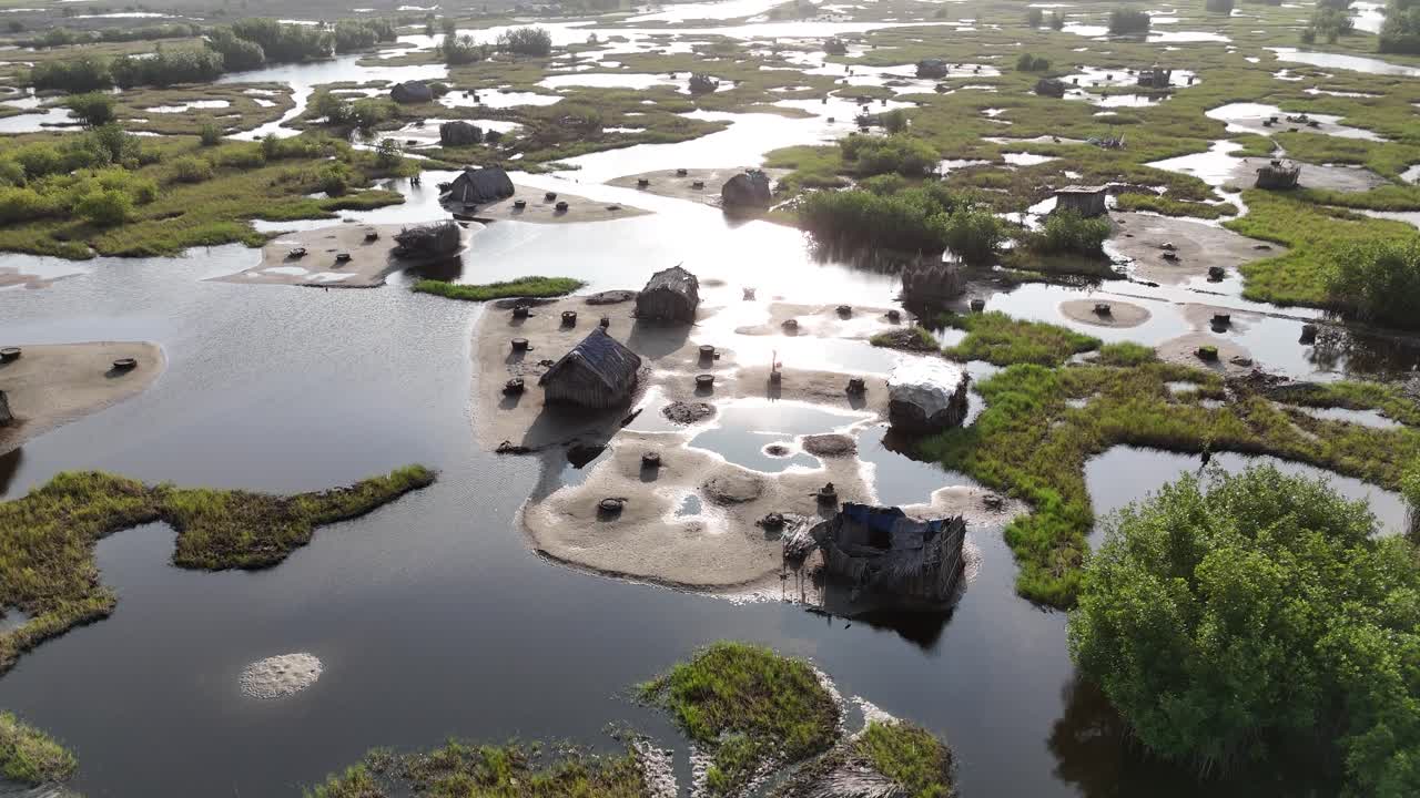 Toma de dron de los marismas costeros en Ouidah, Benín. Muestra cabañas tradicionales con techo de paja rodeadas de sinuosos canales de agua y exuberante vegetación verde