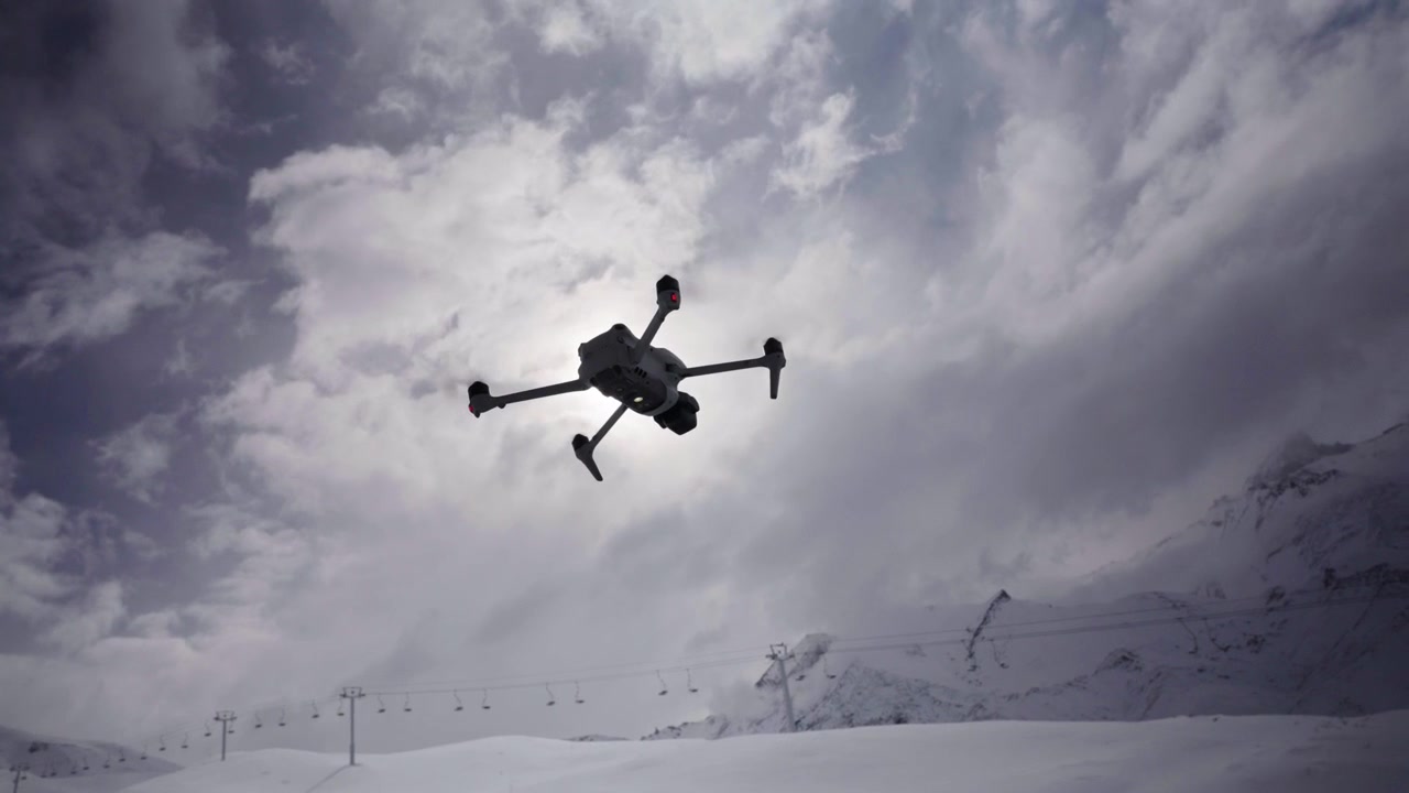 Drone hovering above snowy mountain landscape beneath dramatic cloudy skies, silhouette