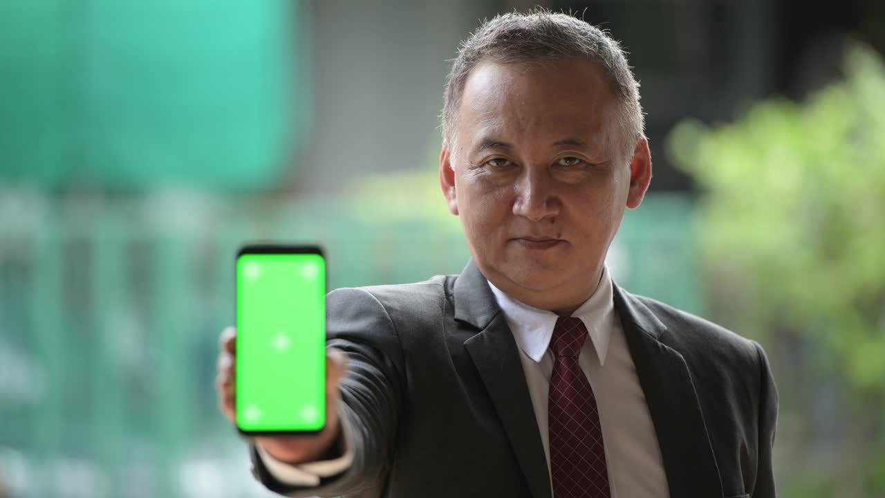 성숙 한 일본인 사업가 가 거리 에서 드폰 을 보여주고 있다