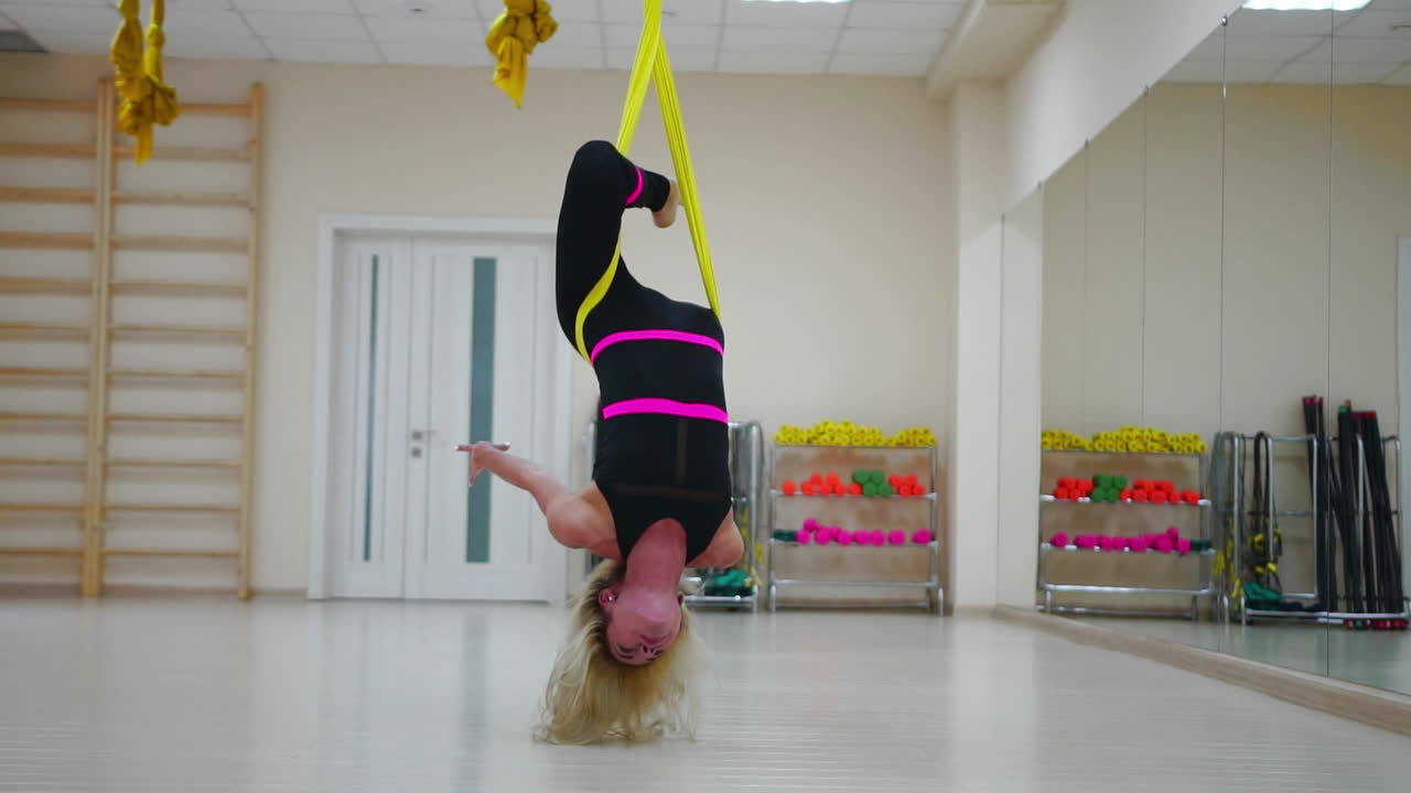 항공 요가에 대한 반중력 수업에 있는 소녀는 캔버스에서 공중에 거꾸로 회전합니다. 슬로우 모션 카메라 촬영