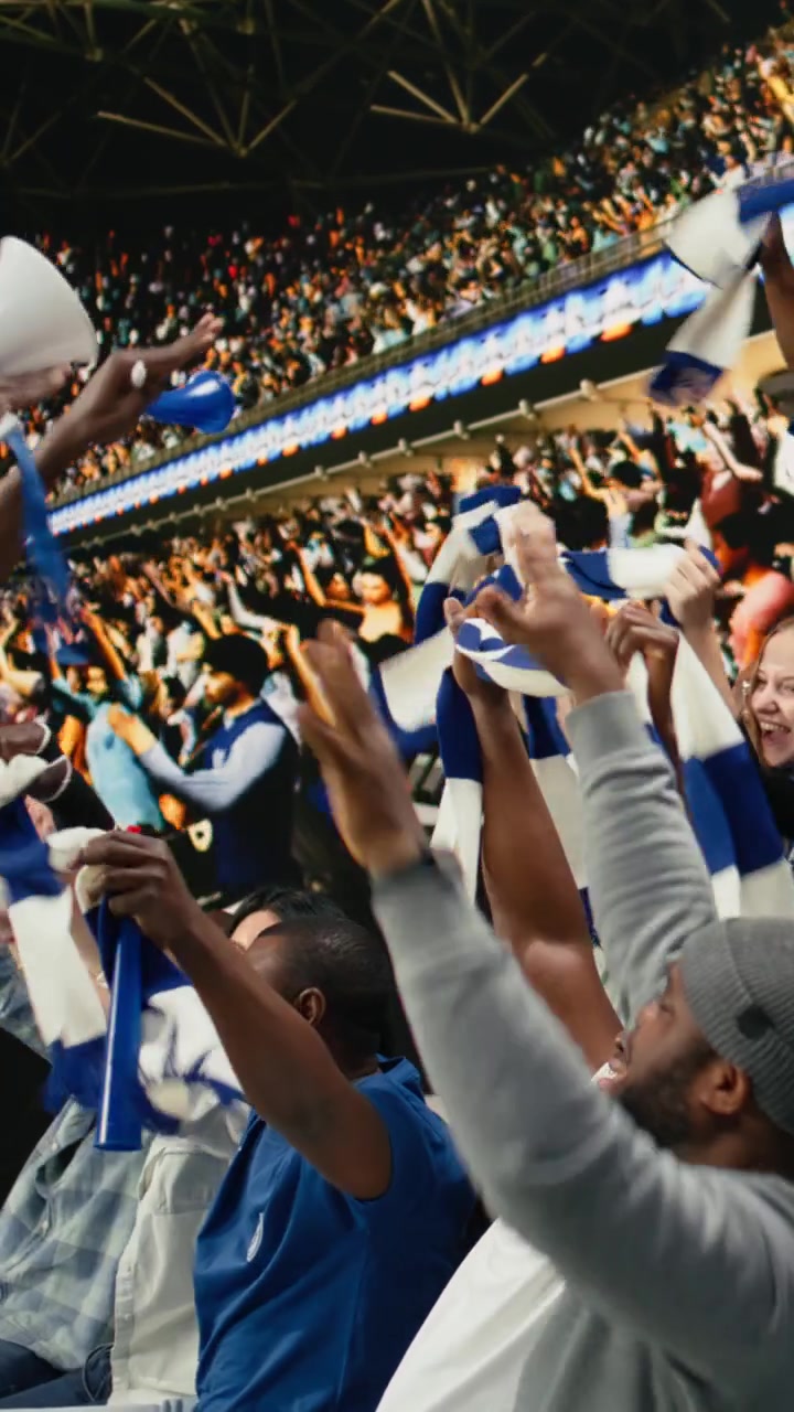 Video vertical: Capo de fútbol del equipo azul de pie sobre la multitud con un megáfono.