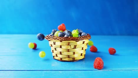 wild berries are pouring out of the falling basket. a basket with different berries falling on a wooden blue table. 4k slow motion video with speed ramp effect.