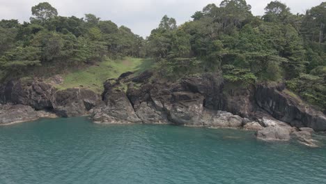 Dron-Dejó-Un-Tiro-De-Camión,-Vista-De-Pájaro-De-La-Costa-De-Roca-De-Granito-En-Una-Isla-Tropical-Con-Exuberante-Bosque-Verde-Y-Océano