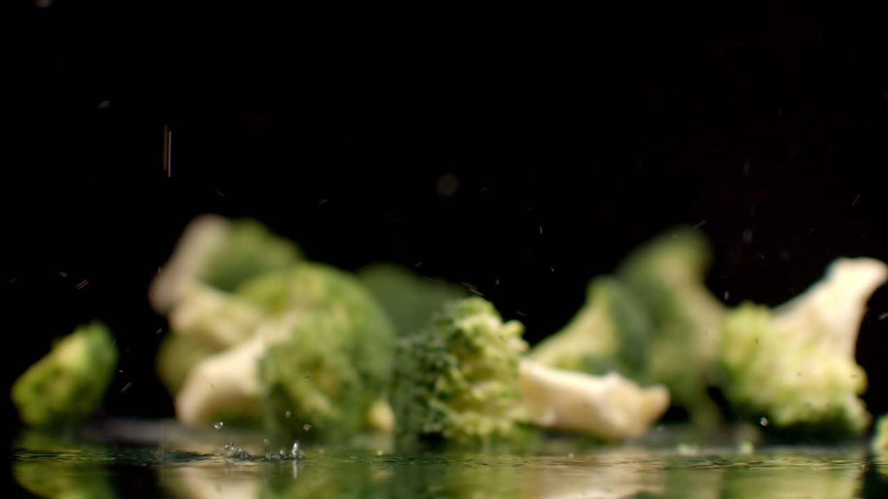Fresh green broccoli fall on a glass with splashes and drops of water in slow motion