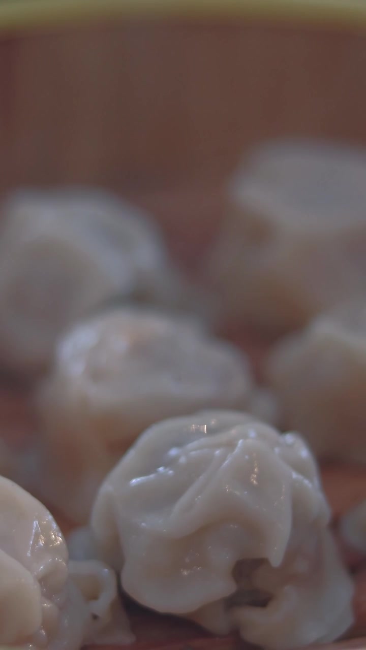 Close-up detail shot steam rising from several siomai (dumplings) inside a bamboo steamer showing a glimpse of authentic traditional dim sum dining style