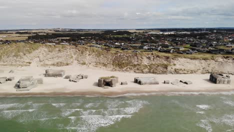 Luftaufnahme-Eines-Wunderschönen-Weißen-Sandstrandes-Mit-Alten,-Verlassenen-Deutschen-Bunkern-Im-Sand,-Wellen-Und-Häusern-In-Der-Ferne