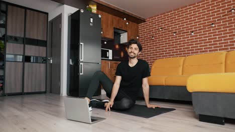 Fitness-male-athlete-practicing-online-exercises-on-floor-a-mat-using-laptop-at-home-in-living-room