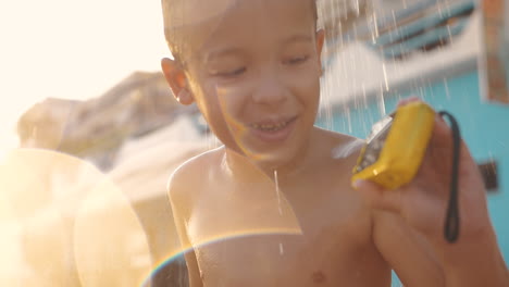 Niño-Tomando-Una-Ducha-En-La-Playa-Y-Viendo-Fotos-Con-Una-Cámara-Impermeable