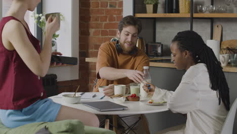 tres compañeros de cuarto desayunando y hablando juntos en la cocina