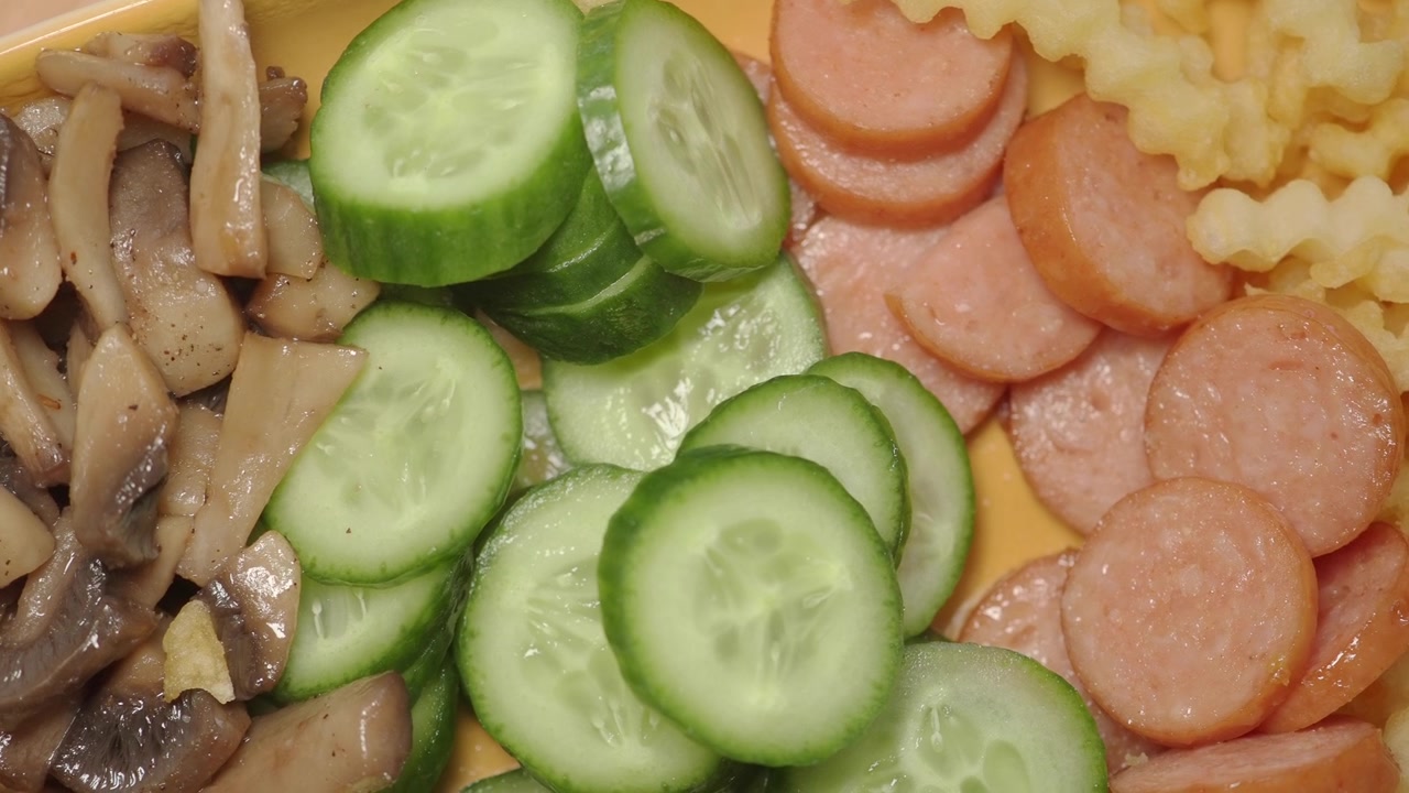 Draufsicht auf einen Teller mit geschnittenen Würstchen, Gurke und Wellenpommes.