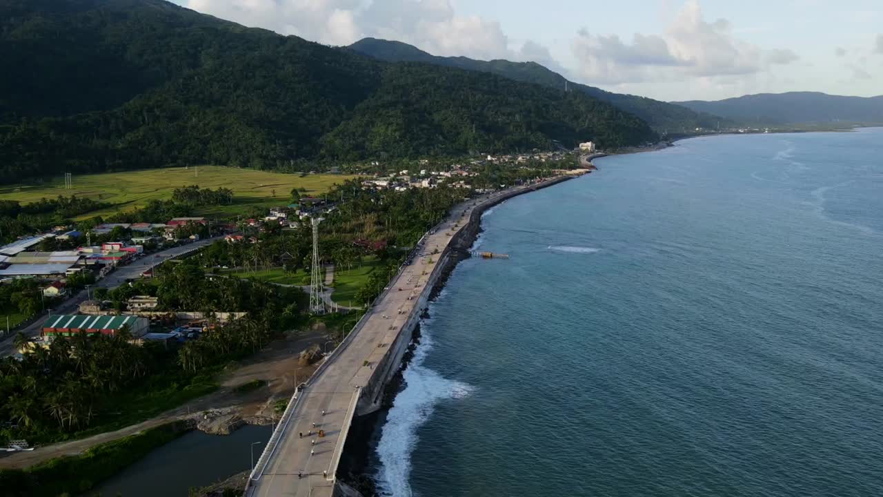 Picturesque aerial hyperlapse of coastal seawall, Virac Boulevard, with turquoise ocean waters and lush mountain backdrop at Catanduanes, Philippines