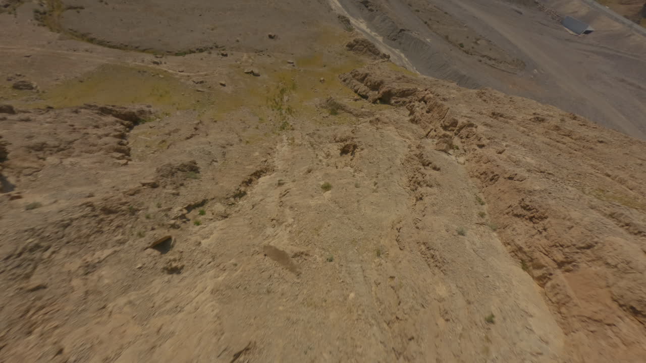 FPV drone descends rocky slope, swings right, and stabilizes parallel to desert floor in Hatta, United Arab Emirates