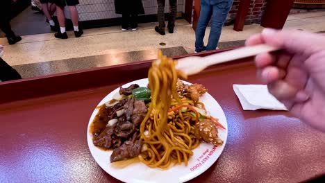 person enjoying noodles with meat at market