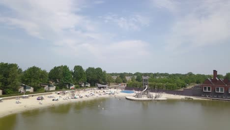 view of 4k drone approaching the shore of the lake with people bathing, in nooitgedacht, the netherlands