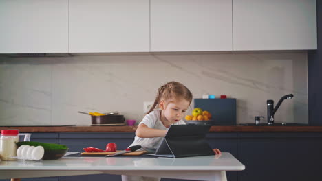 Mädchen-Spielt-Mit-Tablet-Am-Tisch-Mit-Kochzutaten