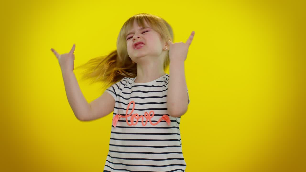 Overjoyed kid showing rock n roll gesture by hands, cool sign, dancing rejoicing in success win