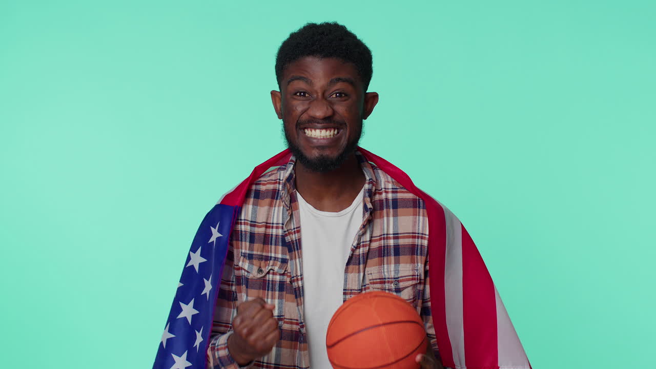 수염이 있는 젊은 남자 농구 팬이 미국 국기를 들고 우승자 제스처를 하고 혼자 춤을 춘다