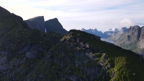 aerial flyover passing over traveler people hiking and walking on reinebringen mountain summit ridge revealing numerous steep peaks and fjord, reine, norway