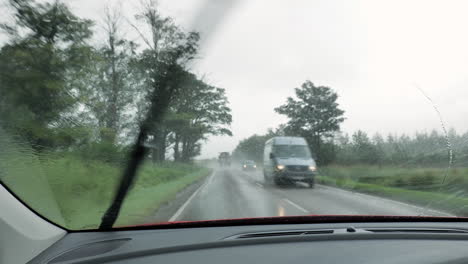 interior view from a red car driving on a right side of the road in heavy rain