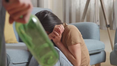 close up of young asian woman victim of violence with bruise on body sits on the floor being scared of a man holding a glass bottle hitting her at home