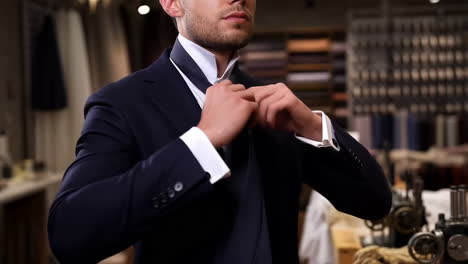 man tying a tie and adjusting his collar in a tailor shop