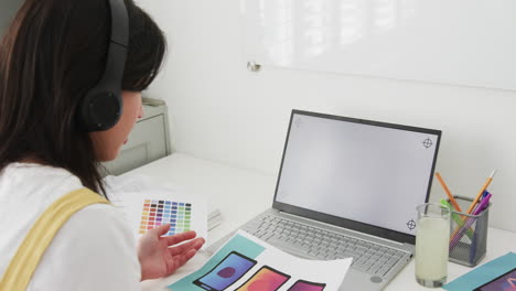 biracial female designer at desk having video call on laptop with copy space on screen, slow motion