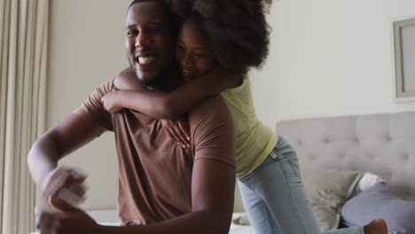 african american daughter jumping on her father and embracing him