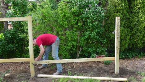 man uses cordless power drill to screw wooden fence, static view