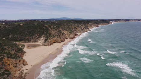 aerial of wild stormy ocean waves under cloudy sky and sandy beach, with cliffs along coastline