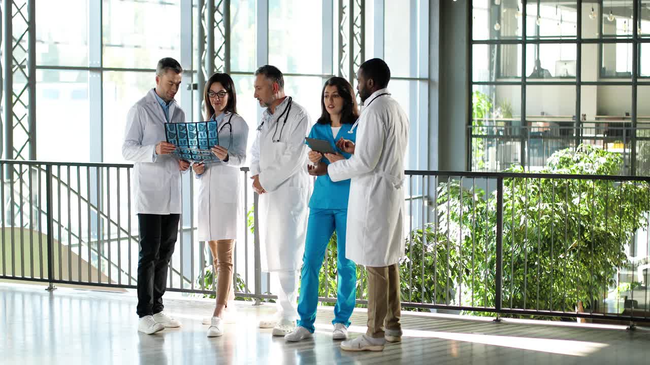 다민족 의사, 남녀, 병원에 서서 x-ray 및 태블릿 장치로 진단에 대해 이야기하고 토론합니다.