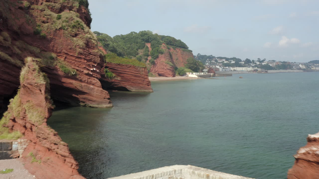 tiro aéreo de drones volando a través de las rocas en dawlish, a lo largo de la costa de devon con acantilados rojos y cuevas marinas con aguas tranquilas en un día soleado