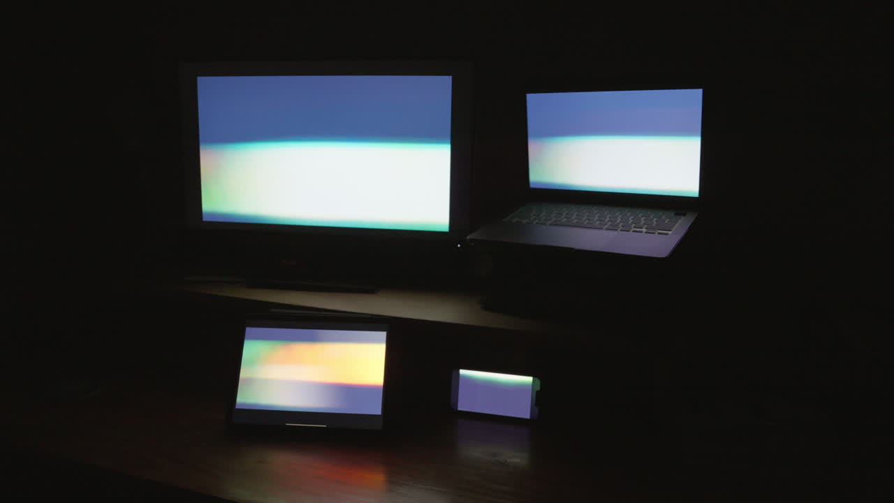 Four digital computer device screens displaying a strobing pattern in a dark room