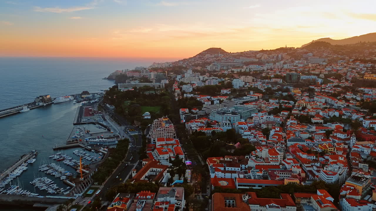 Orange roofs of the multiple white houses located on the top of the mountain slope. Sunset view of the town in the Madeira Islands, Portugal. Top perspective.