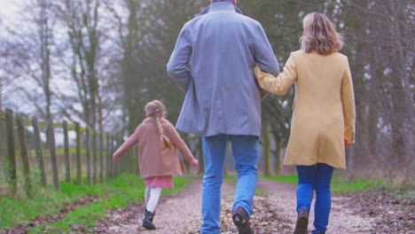 grandparents watching granddaughter skipping ahead on outside walking through winter countryside