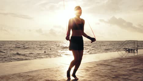 young woman working out on the jump rope against the son by the beach in slow motion. girl jumping on a skipping rope by the sea