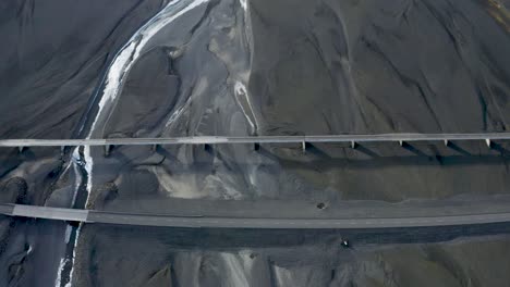 looking down on a bridge in iceland running over flat black lava sand across a glacial runoff river