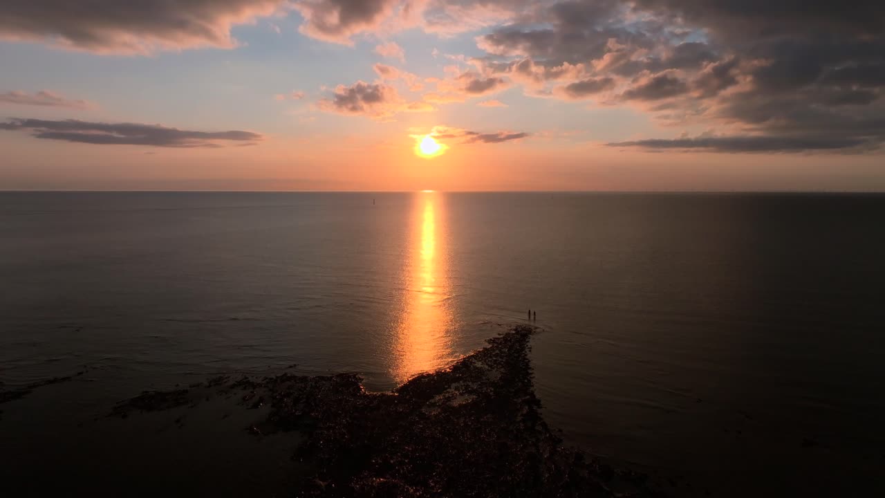 Two Lone Figures Standing On The Tide Line Near Calm Sea At Sunset. Golden Hour. Fleetwood, Lancashire, UK