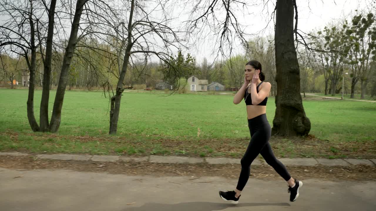 Young fit girl is running with earphones in park in summer, healthy lifestyle, sport conception, side view
