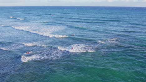 Imágenes-De-Drones-A-Través-De-Las-Aguas-Azul-Verdosas-De-La-Costa-De-Oahu,-Hawaii,-Mientras-Las-Olas-Cubiertas-De-Blanco-Golpean-A-Los-Surfistas-Y-Practicantes-De-Kitesurf-En-Su-Camino-Para-Atrapar-Una-Ola.