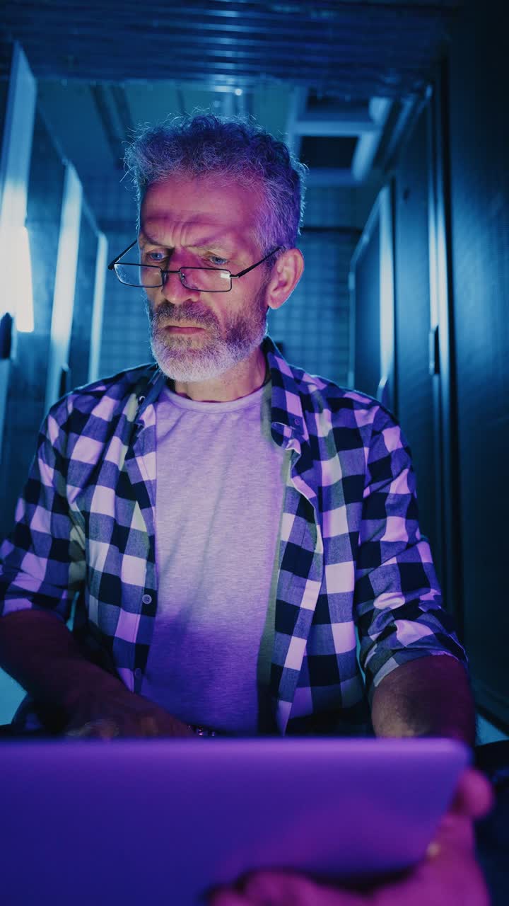 Senior IT Technician Working in a Server Room at Night